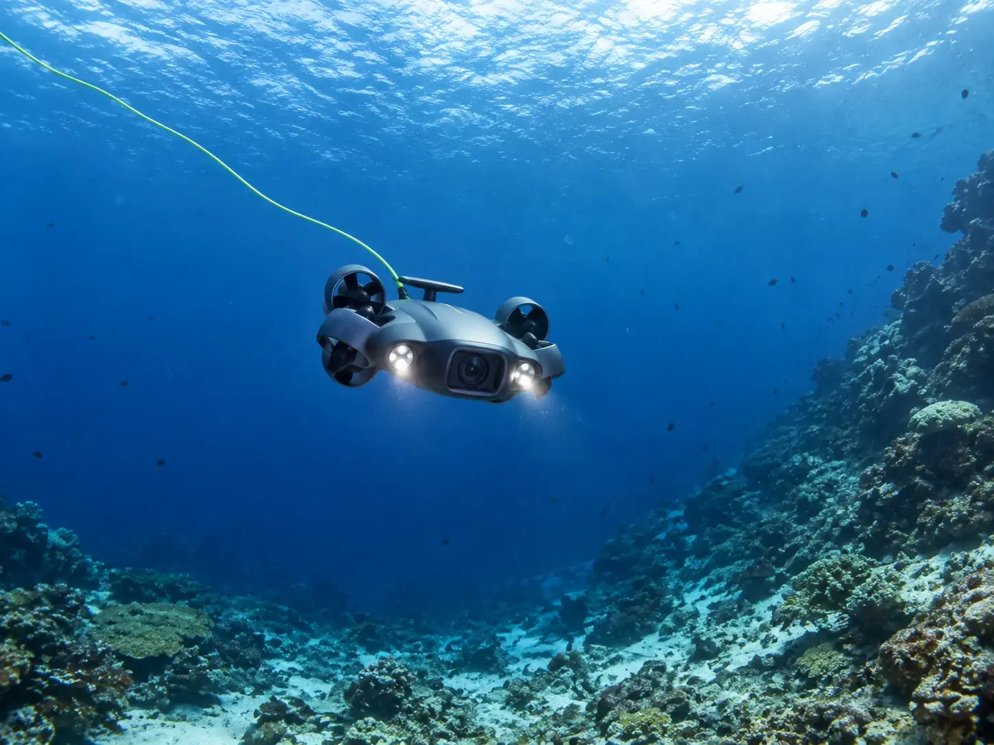 The underwater drone with its lights on, descending along a reef wall into deeper blue water in Curaçao